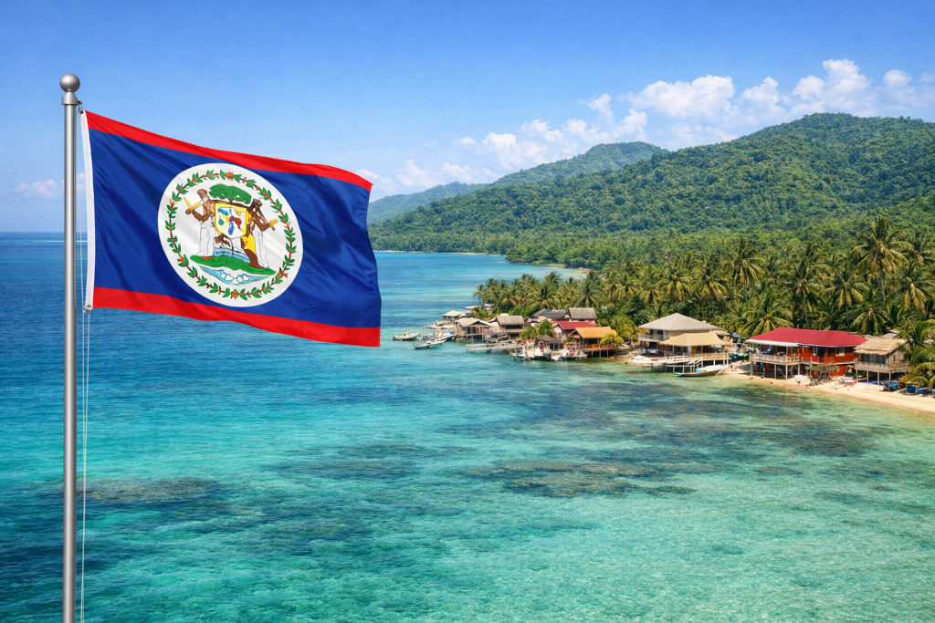 Nationalflagge von Belize mit blauem Grund, roten Streifen und zentralem Staatswappen, links am Fahnenmast wehend, vor tropischer Küstenlandschaft mit türkisfarbenem Meer, Palmen, Stelzenhäusern am Wasser und bewaldeten Hügeln unter blauem Himmel im 16:9‑Format Nationalflagge von Belize mit blauem Grund, roten Streifen und zentralem Staatswappen, links am Fahnenmast wehend, vor tropischer Küstenlandschaft mit türkisfarbenem Meer, Palmen, Stelzenhäusern am Wasser und bewaldeten Hügeln unter blauem Himmel im 16:9‑Format