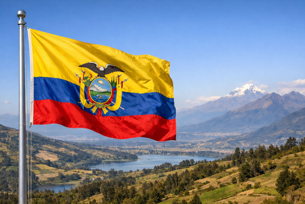 Nationalflagge von Ecuador, links am Fahnenmast wehend, vor weiter Andenlandschaft mit grünen Hügeln, einem See im Tal und schneebedecktem Vulkan im Hintergrund unter klarem blauem Himmel im 16:9‑Format