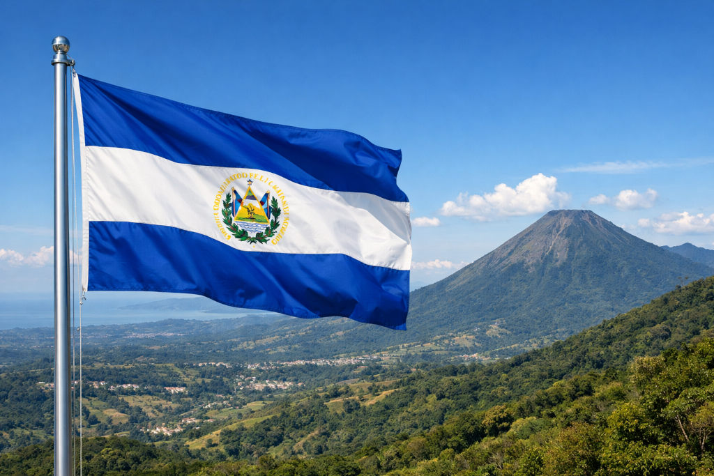 Nationalflagge von El Salvador mit blau‑weißen Streifen und Staatswappen in der Mitte, links am Fahnenmast wehend, vor weiter Landschaft El Salvadors mit grünen Hügeln, Feldern, einer Ortschaft im Tal und einem markanten Vulkan unter klarem blauem Himmel im 16:9‑Format Nationalflagge von El Salvador mit blau‑weißen Streifen und Staatswappen in der Mitte, links am Fahnenmast wehend, vor weiter Landschaft El Salvadors mit grünen Hügeln, Feldern, einer Ortschaft im Tal und einem markanten Vulkan unter klarem blauem Himmel im 16:9‑Format