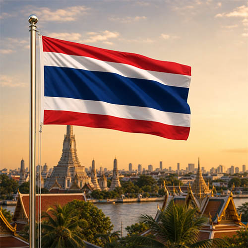 Flagge Thailands vor dem Wat Arun, der Skyline von Bangkok und dem Chao-Phraya-Fluss in warmer Abendstimmung.