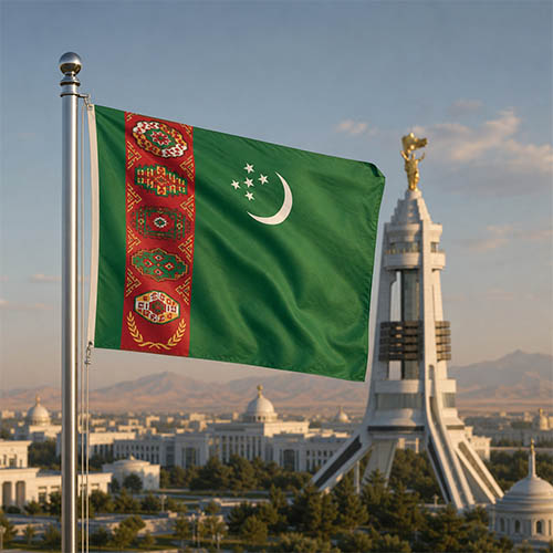 Flagge Turkmenistans vor dem Neutralitätsdenkmal in Aschgabat, den weißen Marmorgebäuden der Hauptstadt und der Karakum-Wüste in warmer Abendstimmung.