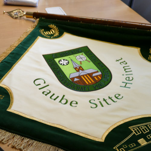 Detailaufnahme der neuen Stickfahne der St. Hubertus Schützenbruderschaft Porz-Urbach von 1926 e.V., mit Wappen, Kirchturm, Zielscheibe, gekreuzten Gewehren, goldenem Jubiläumsemblem und dem Schriftzug 